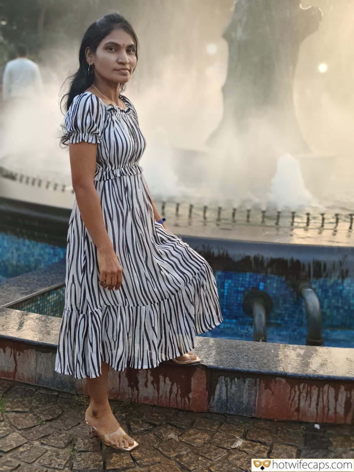 Wife Sharing Submitted by Users 🔥 Humiliation Cuckold Stories hotwife caption: A woman in a striped dress stands confidently near a misty fountain in a public park, exuding an alluring presence that captivates the observer. A Day at the Fountain: Her Confident Stroll